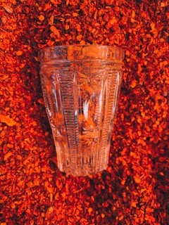 A clear, intricately designed glass is placed on a bed of vibrant red crushed chili peppers, creating a striking contrast between the transparent glass texture and the rich, colorful peppers.