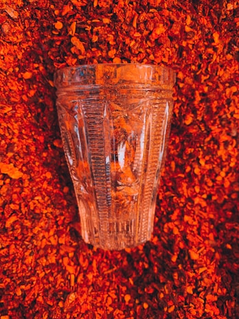 A clear, intricately designed glass is placed on a bed of vibrant red crushed chili peppers, creating a striking contrast between the transparent glass texture and the rich, colorful peppers.