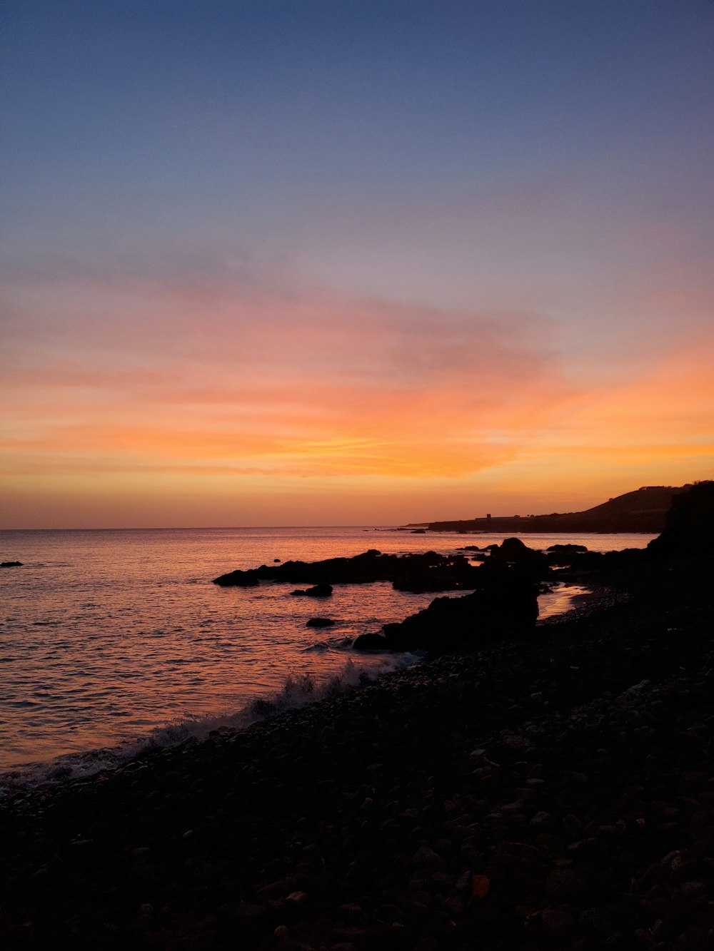 silhouette of rocks on sea during sunset