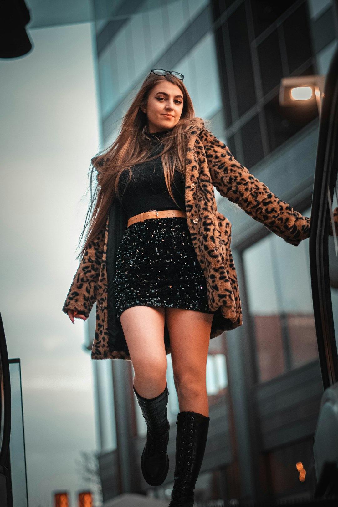 woman in black and brown leopard print coat standing near white wall