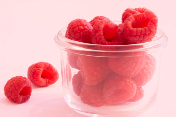 Bright red raspberry powder spilling from a small glass jar onto a wooden table.
