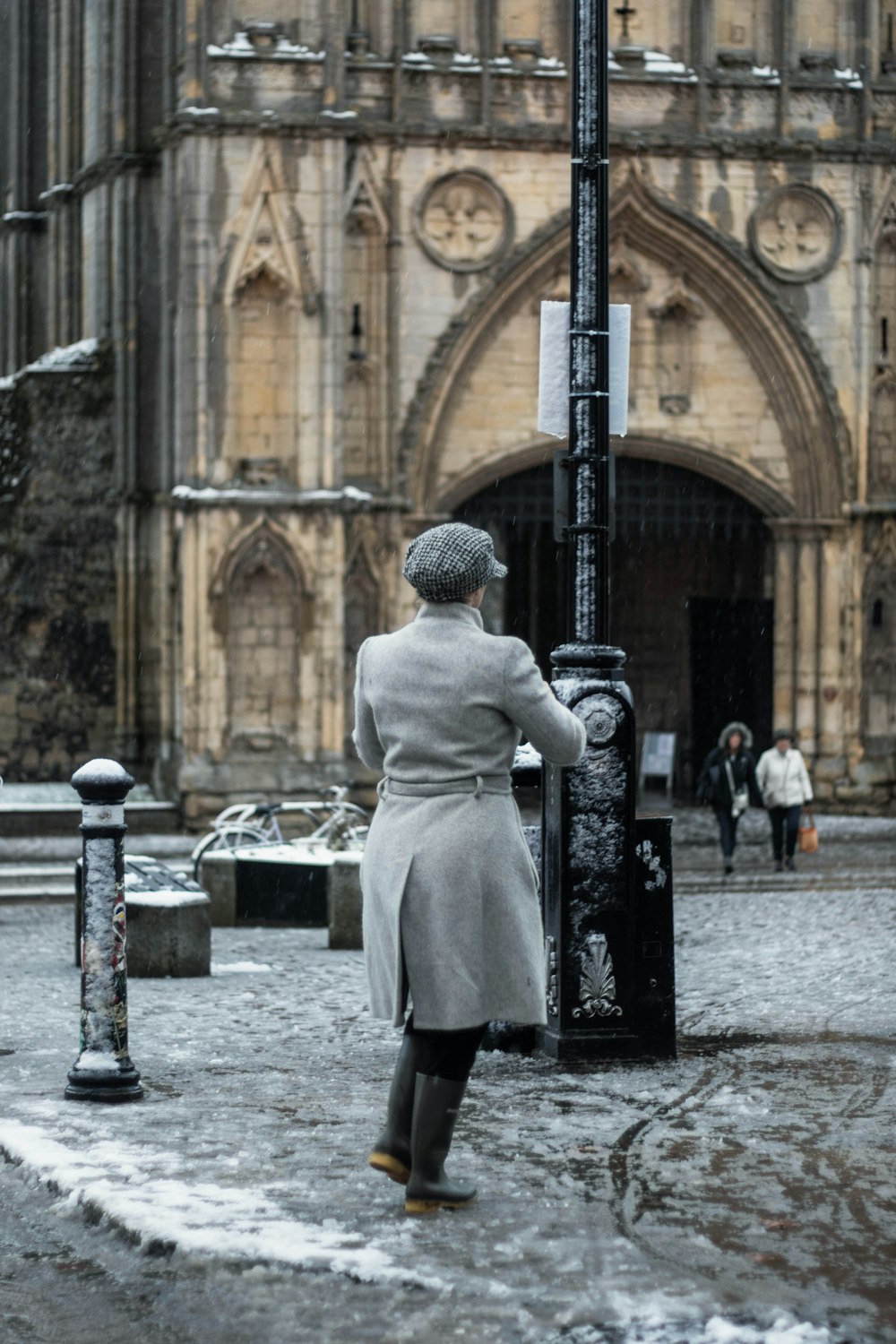 Homme en manteau blanc debout près d’un poteau en métal noir pendant la journée