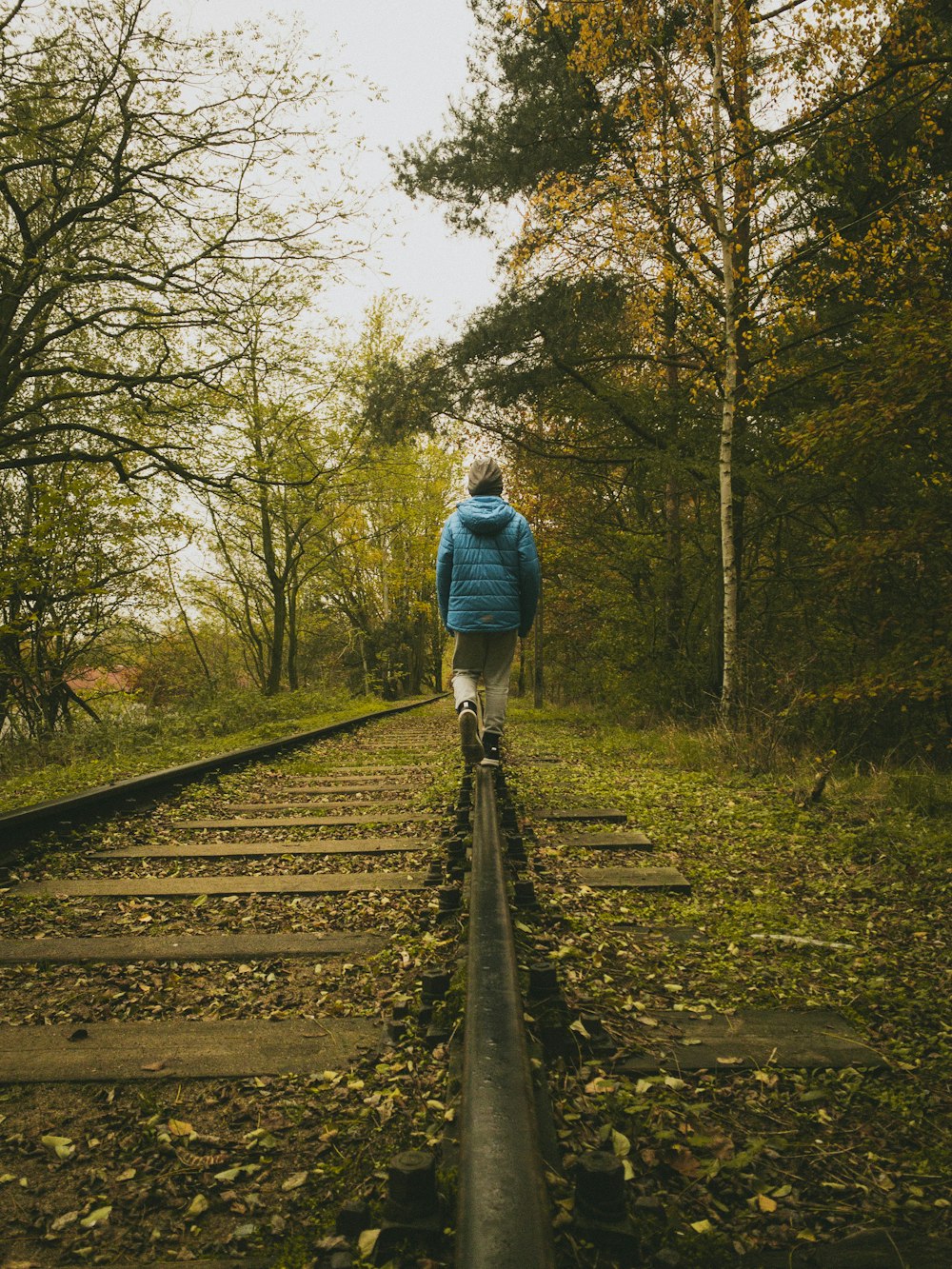 homme en veste bleue marchant sur le rail de train pendant la journée