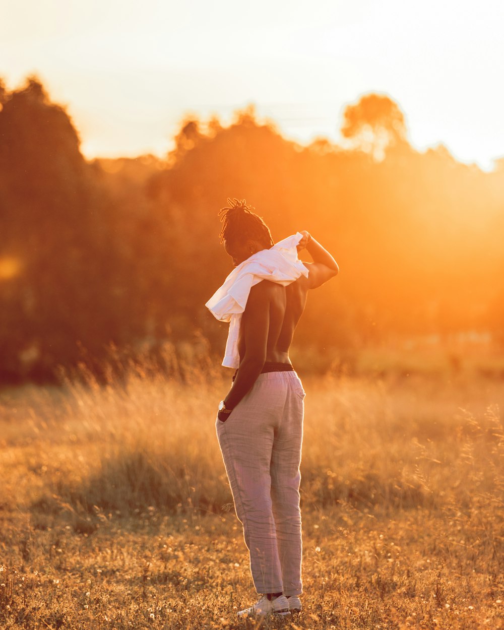 woman in white long sleeve shirt and white pants standing on green grass field during sunset