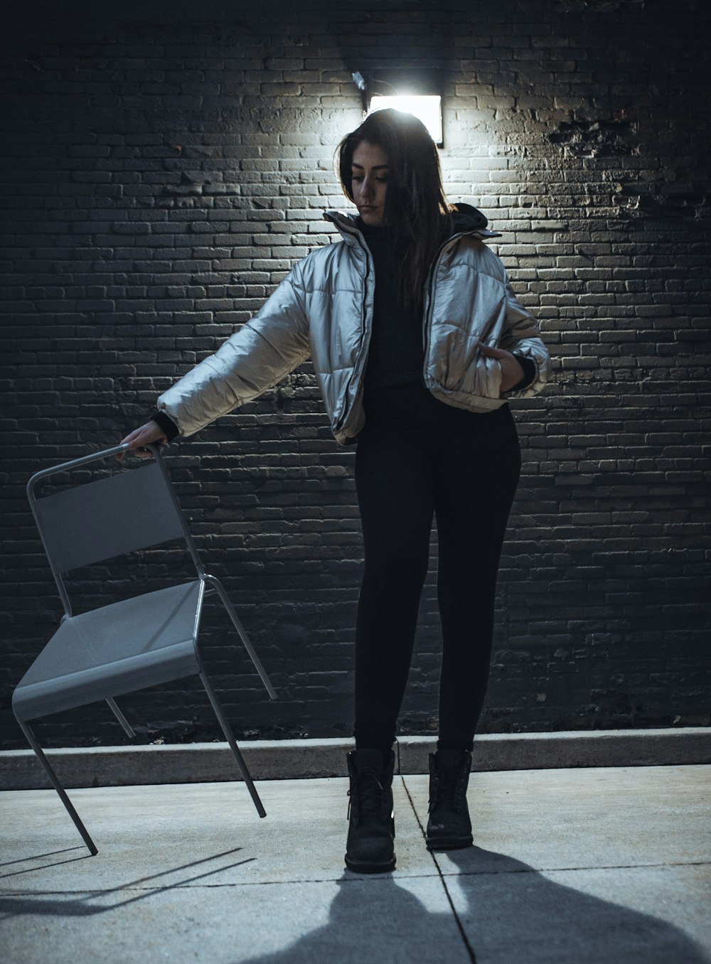 woman in blue denim jacket and black pants standing beside black brick wall