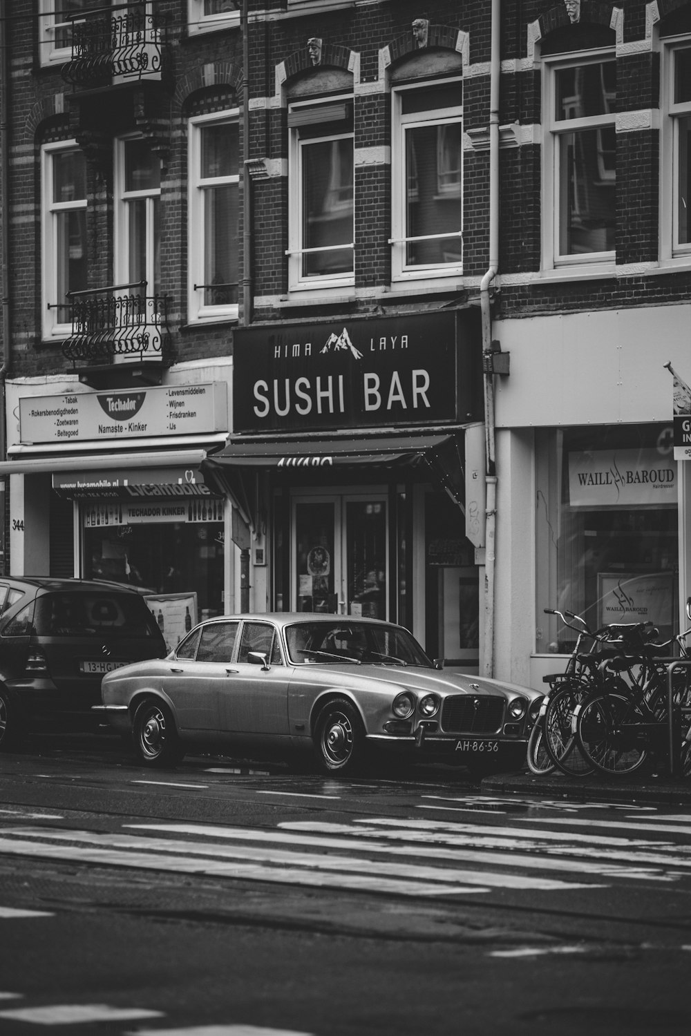 grayscale photo of classic car parked beside building