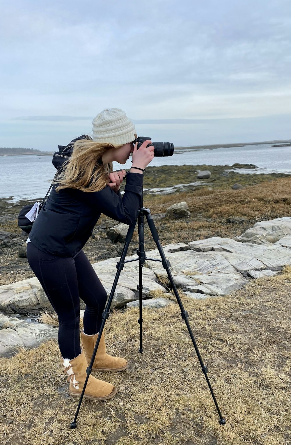 woman in black jacket and blue denim jeans sitting on rock near sea during daytime