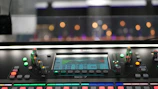 Close-up of broadcast-quality audio mixer with glowing controls in a dark studio.