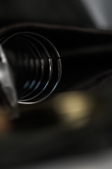 A close-up of a black coiled object, likely a spring, with soft focus and muted lighting. The image is mostly dark with hints of metallic reflections.