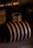 A rusted, large metal coil lies horizontally. The background is dark and out of focus, highlighting the corroded texture. The lighting is warm, casting dramatic shadows on the surface.