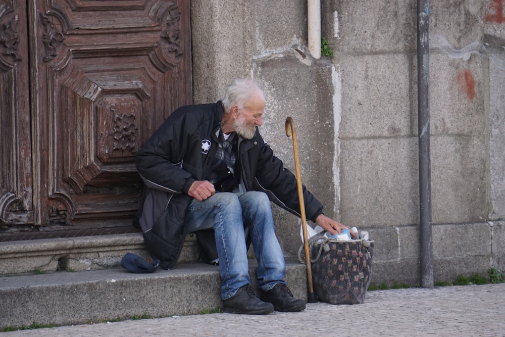 man in black jacket and blue denim jeans sitting on concrete bench