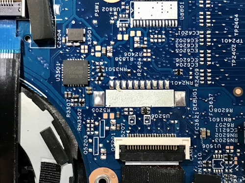 A detailed view of a blue printed circuit board with various electronic components such as capacitors, resistors, and integrated circuits. The board features visible traces and connections, along with labeled components and reference numbers.