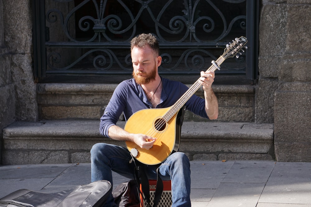 homme en chemise à manches longues rayée bleue et blanche jouant de la guitare assis sur les escaliers