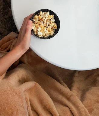 A cozy scene of a hand holding a popcorn bucket next to a smartphone with a delivery app open.