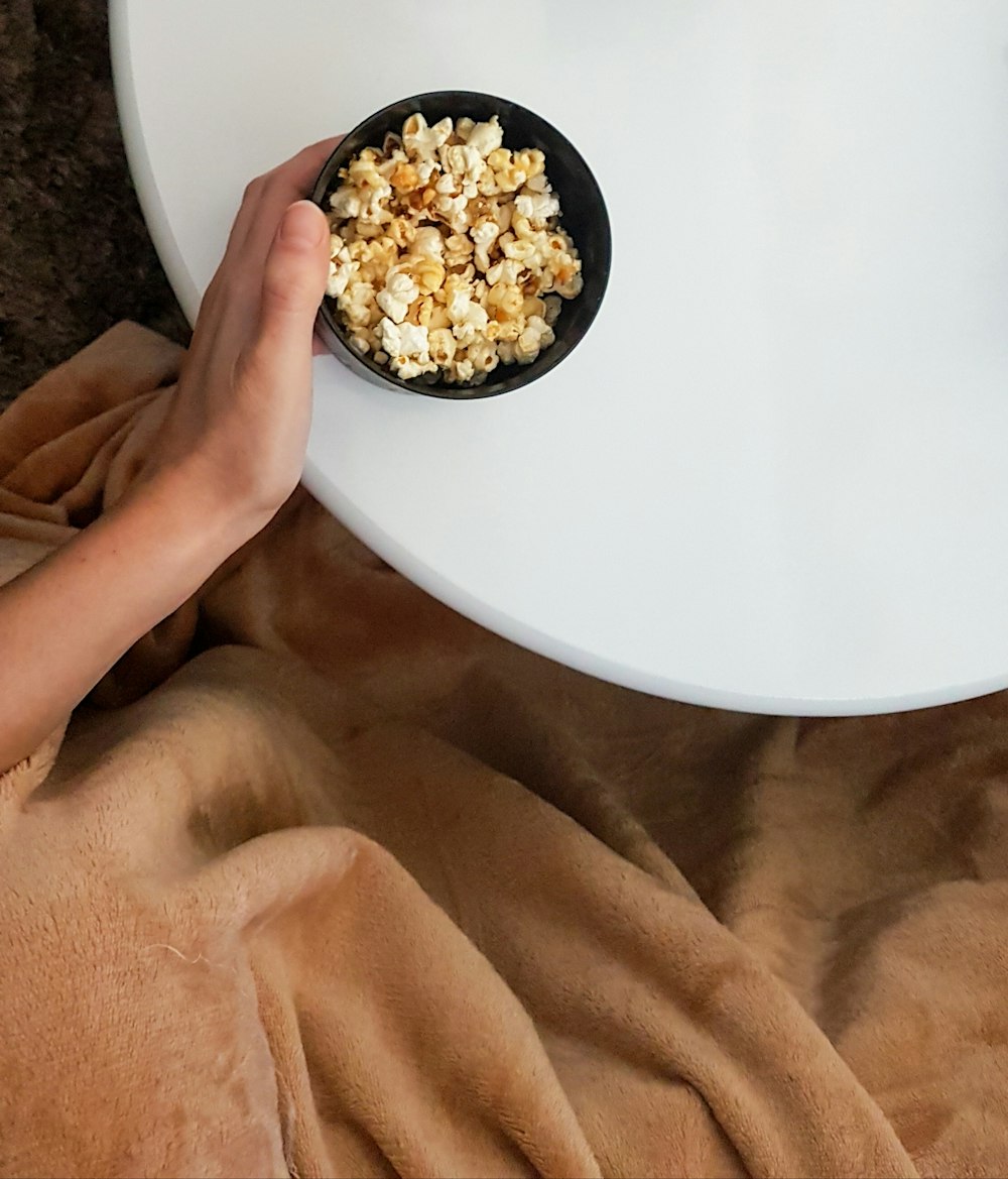 person holding white ceramic plate with popcorn
