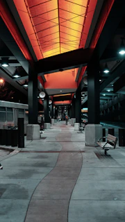 A futuristic bus station with streamlined shelters and integrated digital ticket kiosks illuminated at dusk.