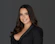 Portrait of a confident businesswoman smiling against a dark, elegant office background.