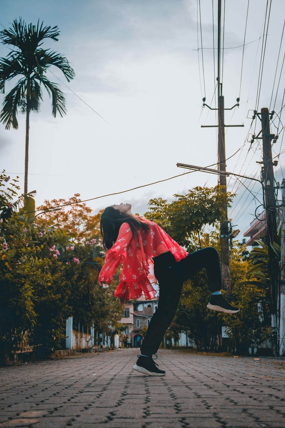 woman in red dress shirt and black pants jumping on street during daytime