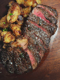 Close-up of a perfectly grilled steak topped with herb butter and served with roasted potatoes.