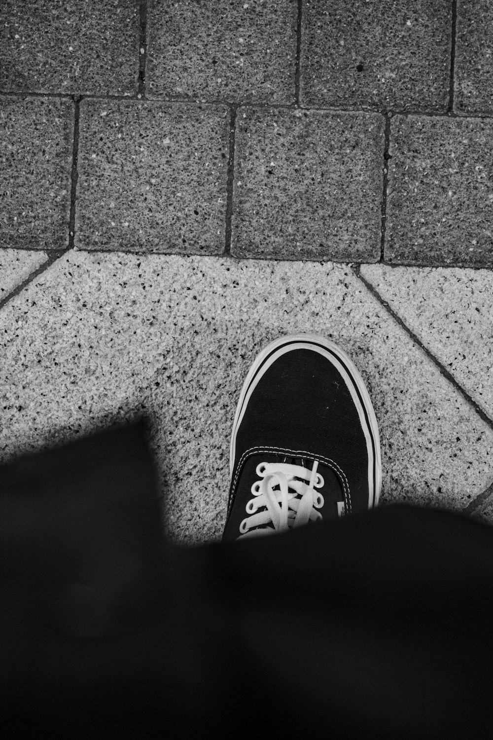 personne portant des baskets noires et blanches debout sur un trottoir en béton gris