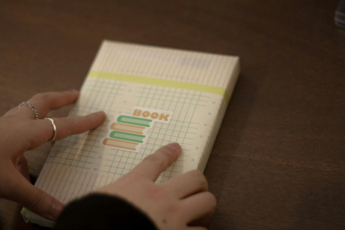 A Girl Scout troop leader writing cookie booth sign-ups on a white and yellow ruled paper with a pen.