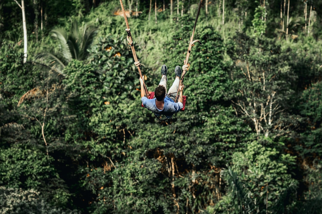 man in blue shirt and blue denim jeans riding on swing