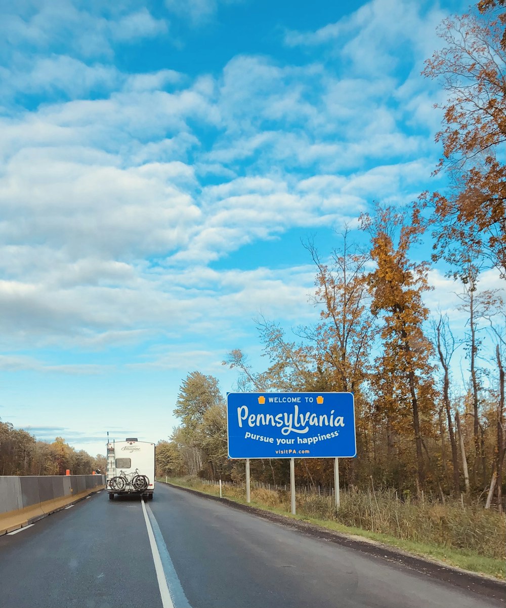 blue and white road sign near trees during daytime