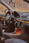 The interior of a luxury car featuring a steering wheel with a logo, a dashboard with a digital display, and a wooden trim. The gear shift and various control knobs are visible, along with a keychain hanging from the ignition.