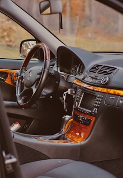 The interior of a luxury car featuring a steering wheel with a logo, a dashboard with a digital display, and a wooden trim. The gear shift and various control knobs are visible, along with a keychain hanging from the ignition.