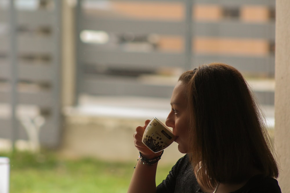 woman in black shirt drinking from white ceramic mug