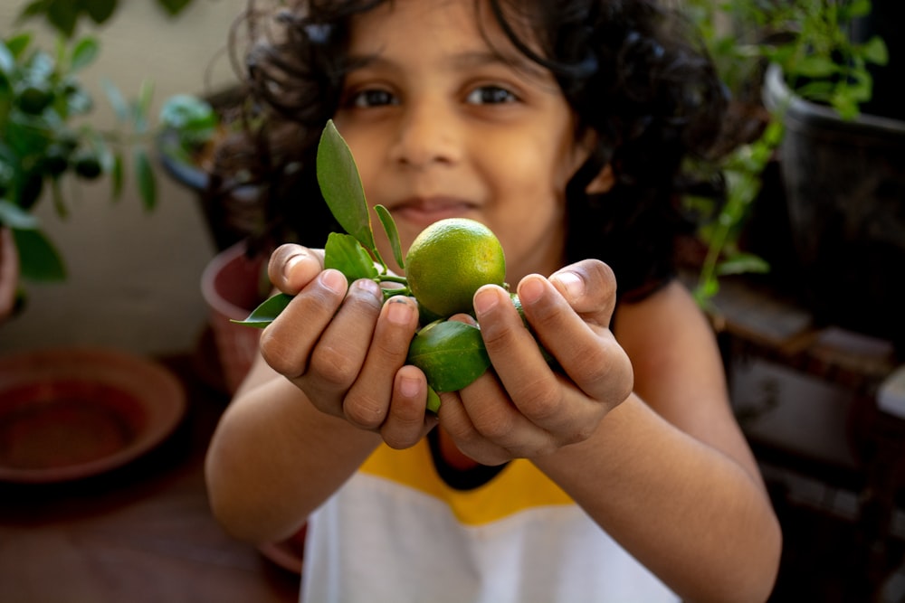 girl in white shirt holding green round fruit