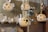 Several ceramic lamps with spherical, perforated designs hang from ropes. In the background, there are shelves displaying various plates and dishes with floral patterns. The setting appears to be a cozy, handcrafted decor store or pottery shop.
