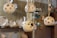 Several ceramic lamps with spherical, perforated designs hang from ropes. In the background, there are shelves displaying various plates and dishes with floral patterns. The setting appears to be a cozy, handcrafted decor store or pottery shop.