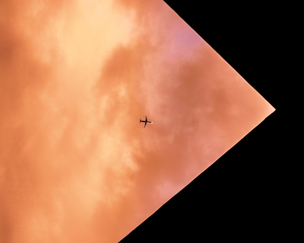silhouette of airplane on mid air under orange sky
