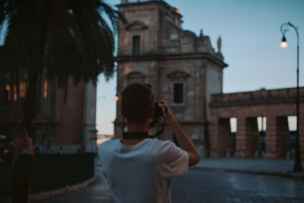 man in white t-shirt taking photo of brown concrete building during daytime