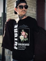 A man outdoors wearing a fun, bold Christian-themed tee, standing against a backdrop of trees and sunlight.