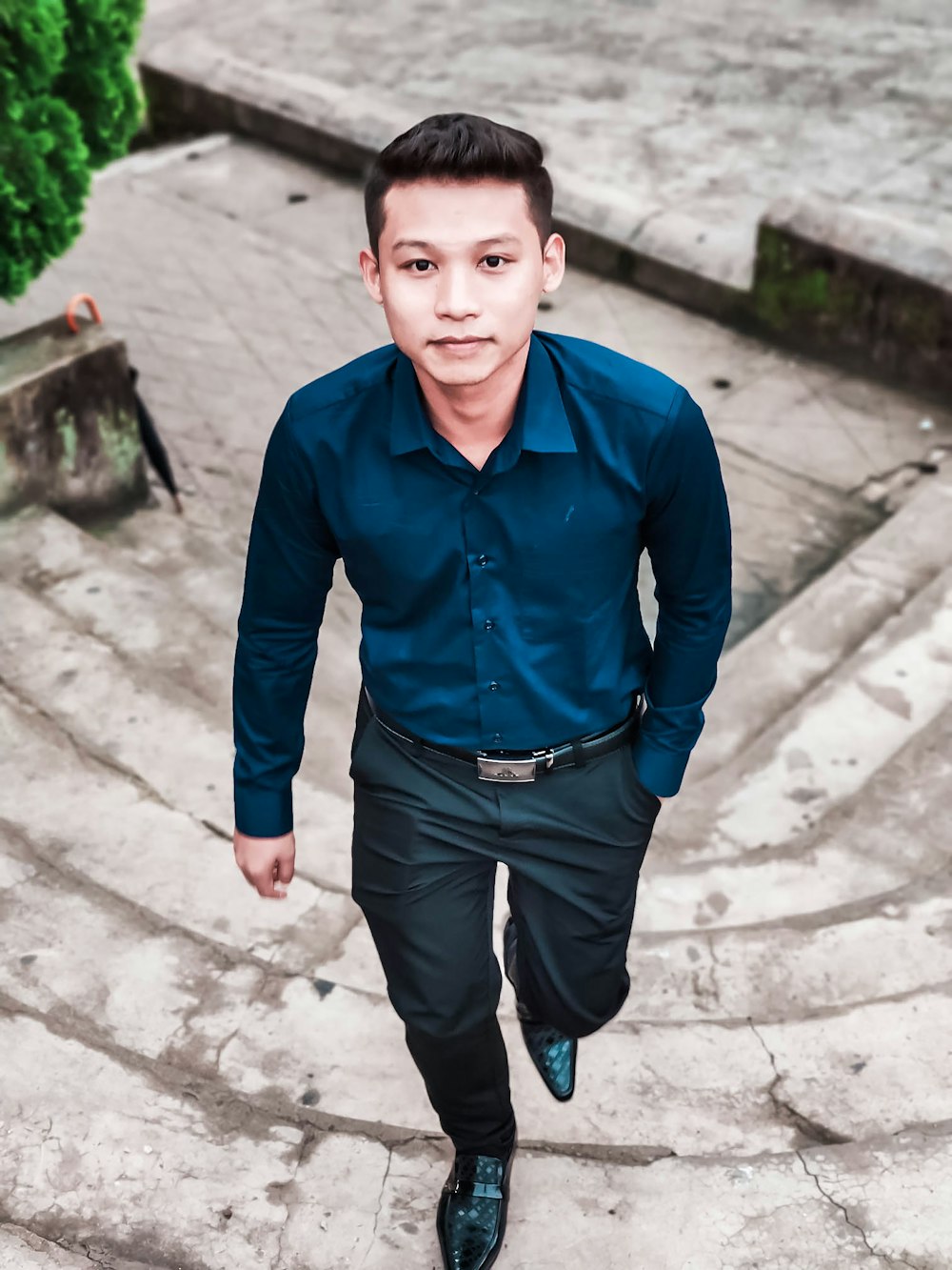 man in blue dress shirt and black pants standing on gray concrete floor during daytime