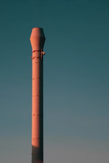 An industrial air emission control device installed on a factory chimney against a clear blue sky.