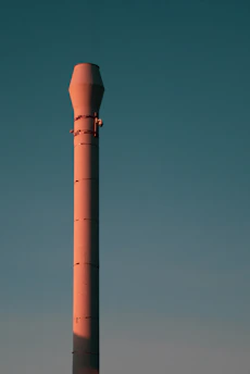 An industrial air emission control device installed on a factory chimney against a clear blue sky.