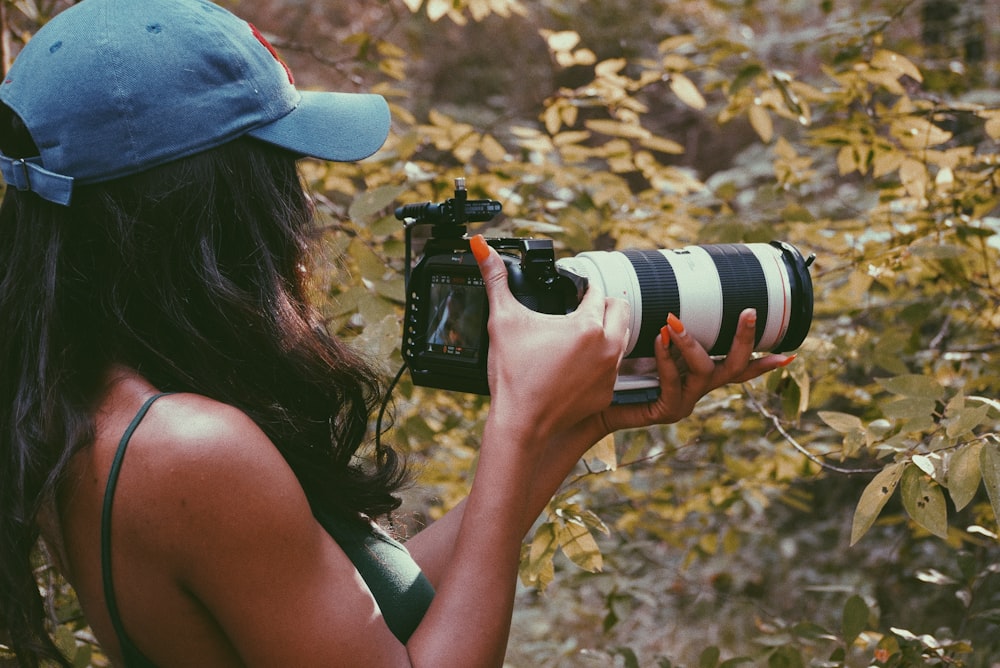 woman in blue cap holding black and white dslr camera
