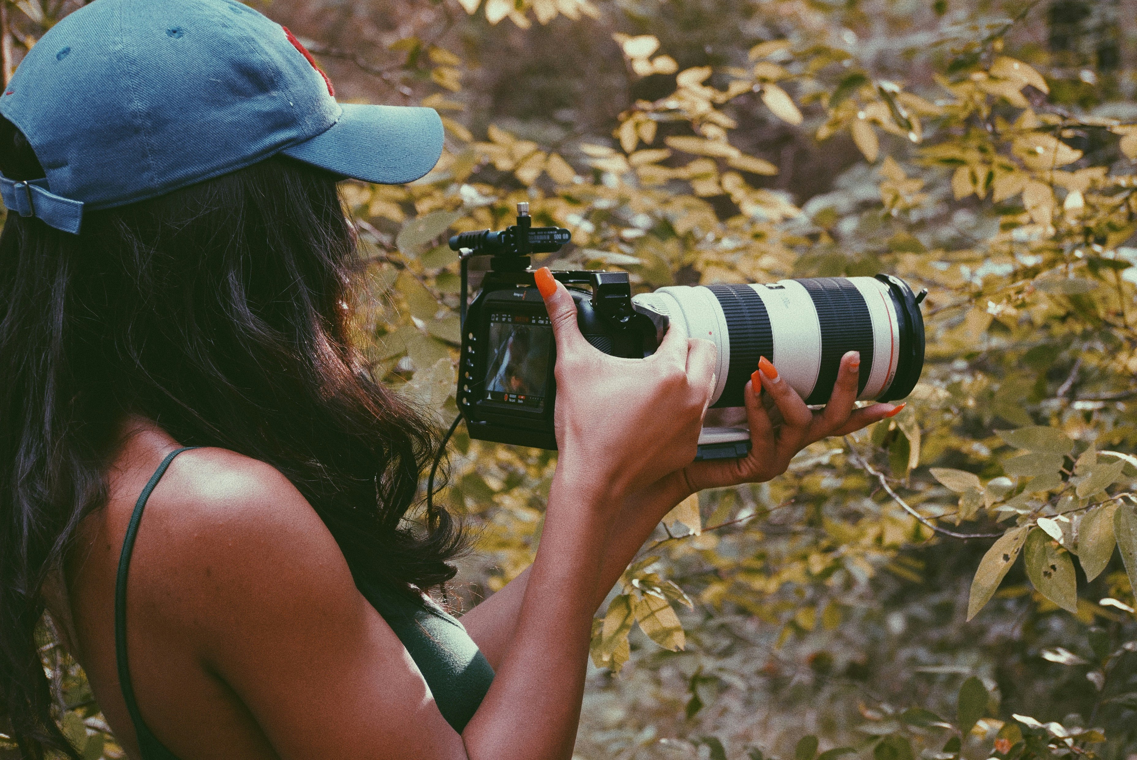 woman in blue cap holding black and white dslr camera