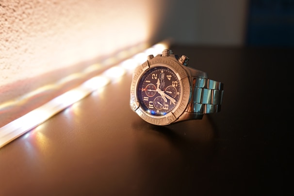 A modern metal bracelet watch reflecting light on a wooden surface.