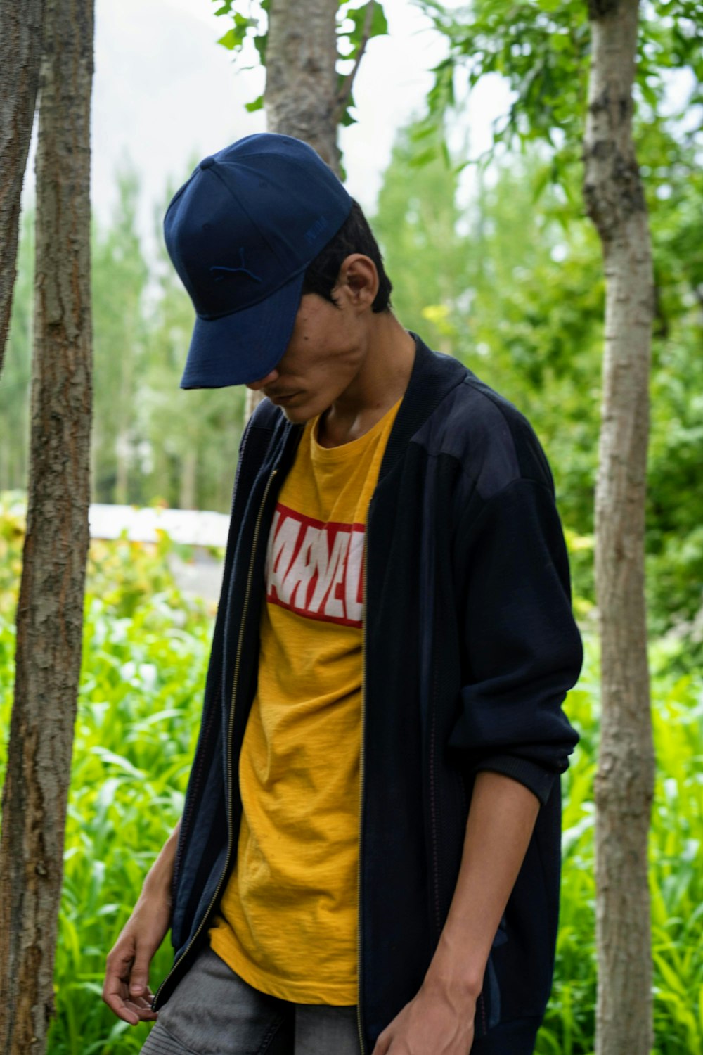 man in blue and yellow jacket wearing black cap standing near brown tree during daytime