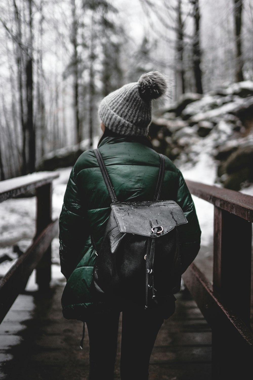 person in black leather jacket and gray knit cap standing on brown wooden bridge during daytime