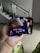 A hand holding a package of Parle Fab! Bourbon biscuits, with a blurred background that includes a staircase and a black chair. The biscuit packaging is primarily purple with images of chocolate biscuits on it.
