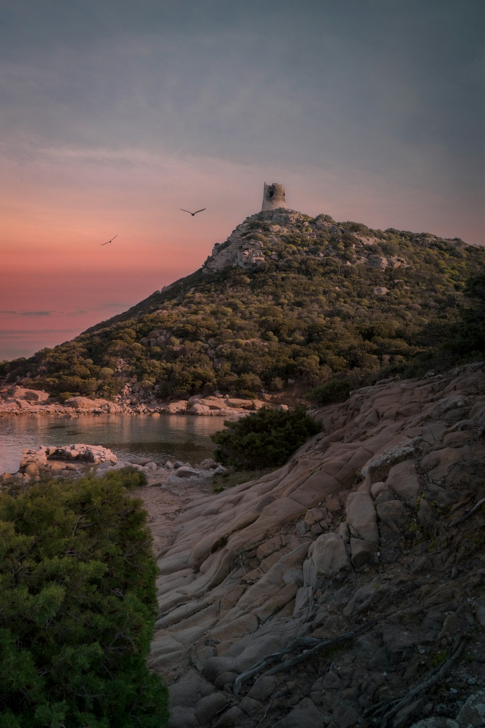 farol branco na colina rochosa marrom perto do corpo de água durante o pôr do sol