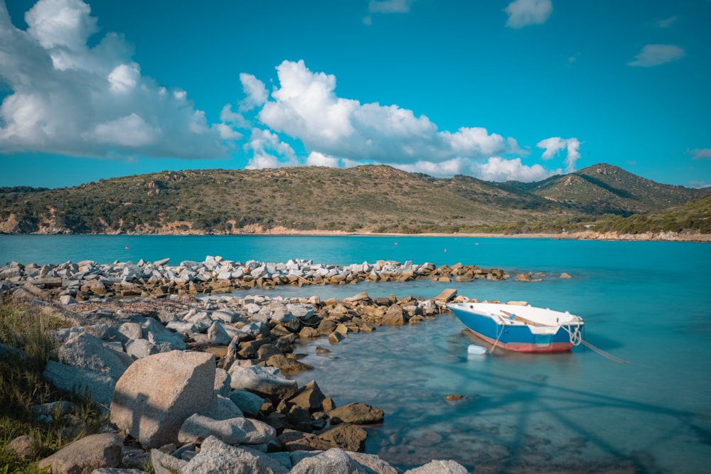 white and red boat on water near gray rocks during daytime