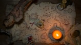 A vintage-style treasure map lies on a wooden surface, illuminated by a lit candle. The map features detailed sketches of landscapes, a ship, and a compass rose, with a red dotted line indicating a path to a marked treasure chest. Scattered around the map are antique coins, a rolled-up scroll, a ring, and decorative jewelry with a red gem.