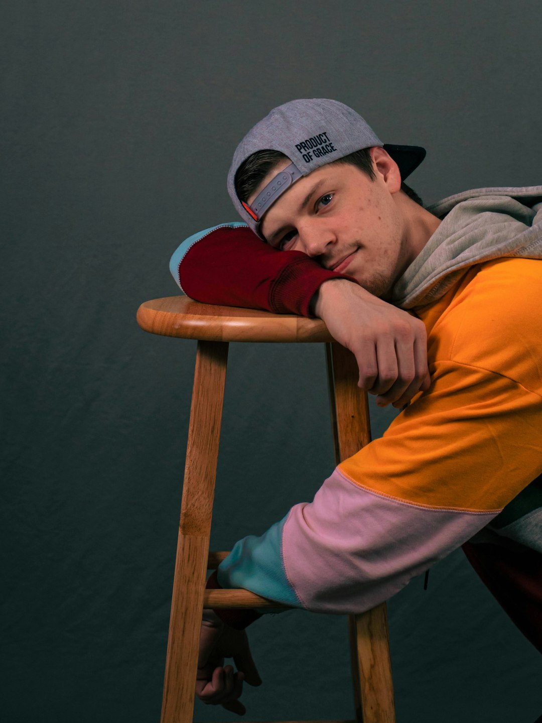 man in orange and gray hoodie and gray cap sitting on brown wooden chair