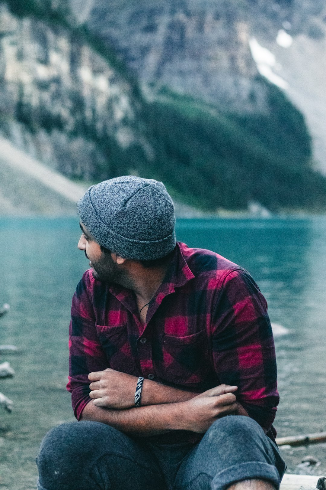 man in red and black jacket wearing gray knit cap standing near body of water during